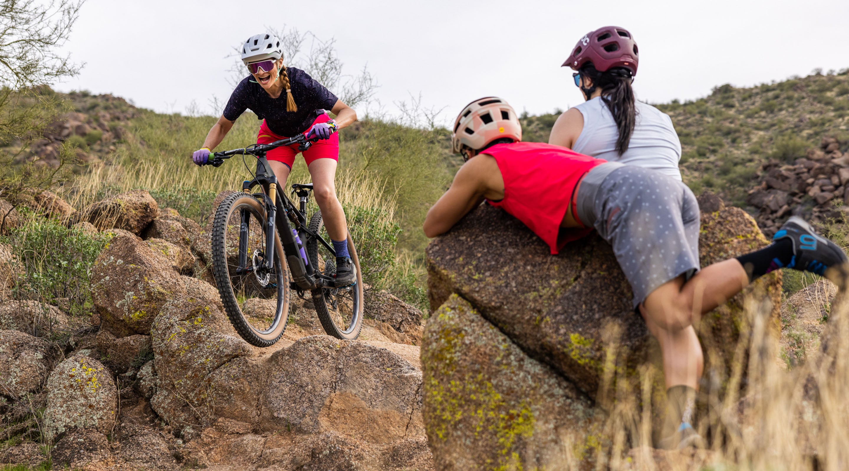 Two women watching another mountain biker ride a rock drop