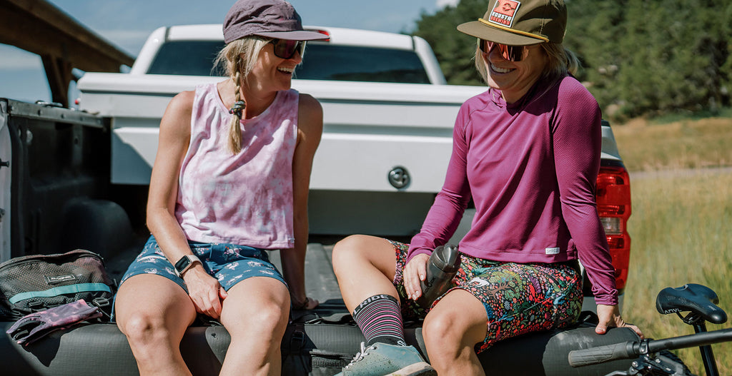 Two women sitting in the back of a truck bed laughing 