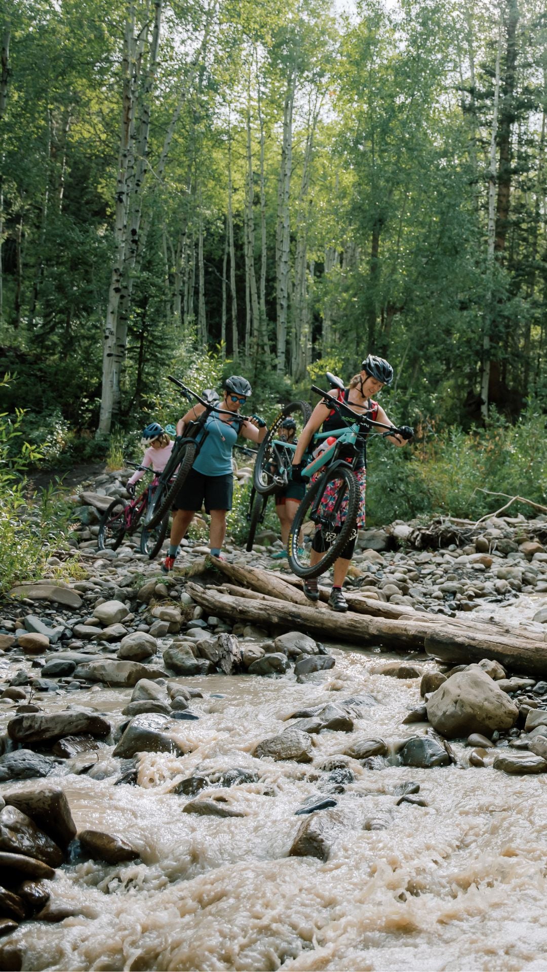 Women crossing river carrying their mountain bikes