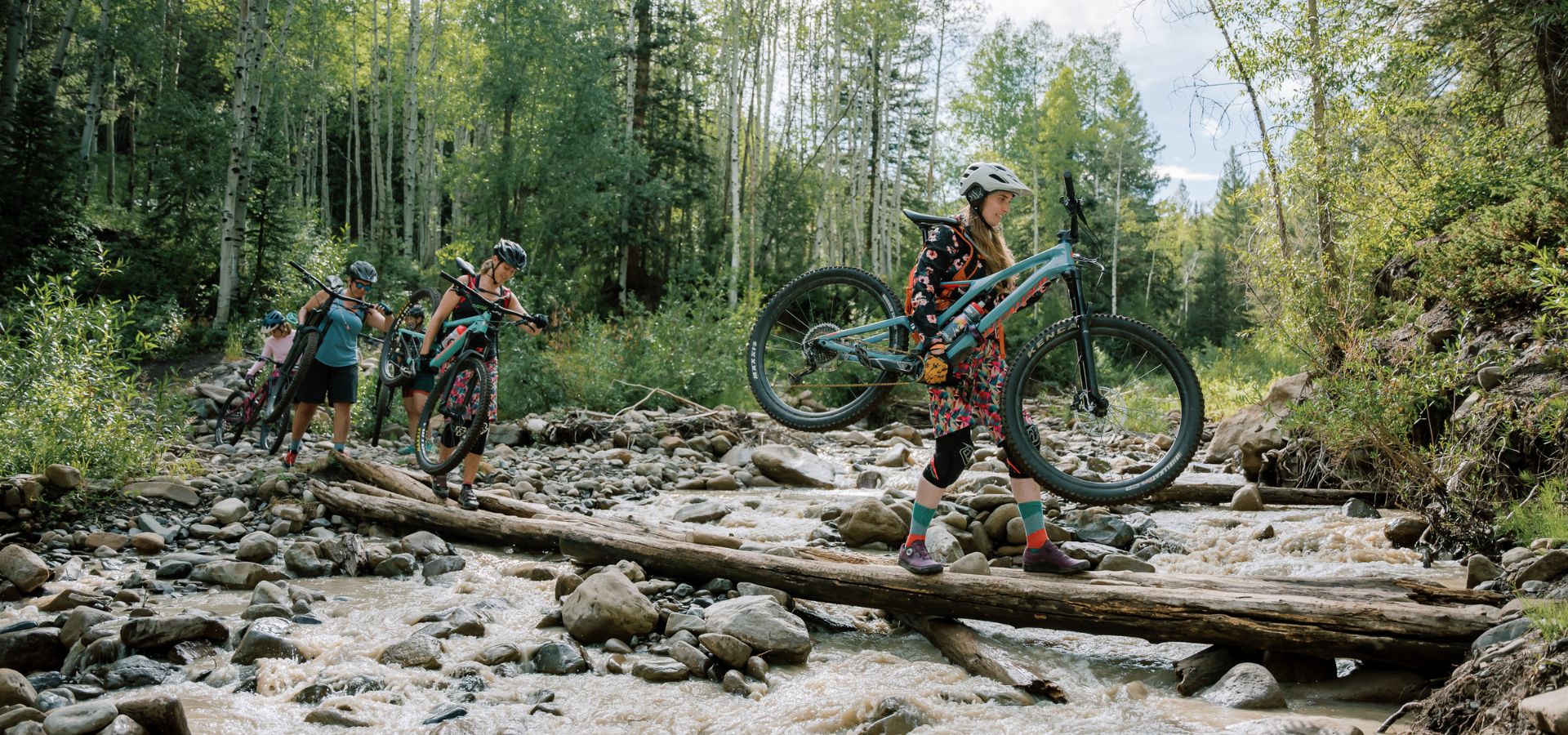 Women crossing river carrying their mountain bikes